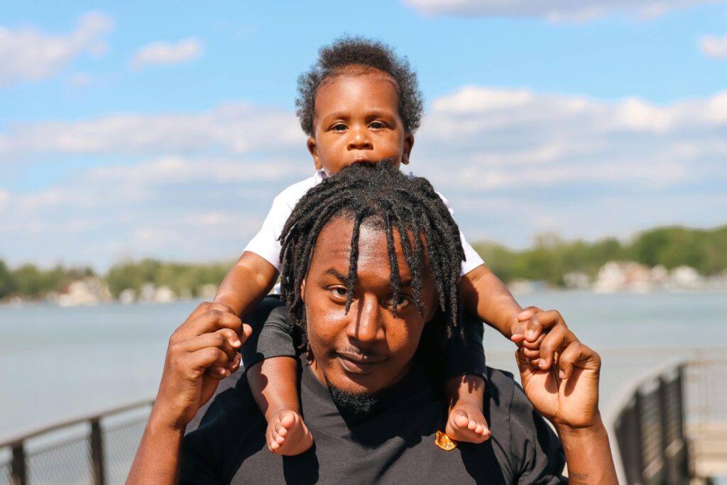A joyful moment of a father carrying his son on shoulders by Walled Lake, MI.