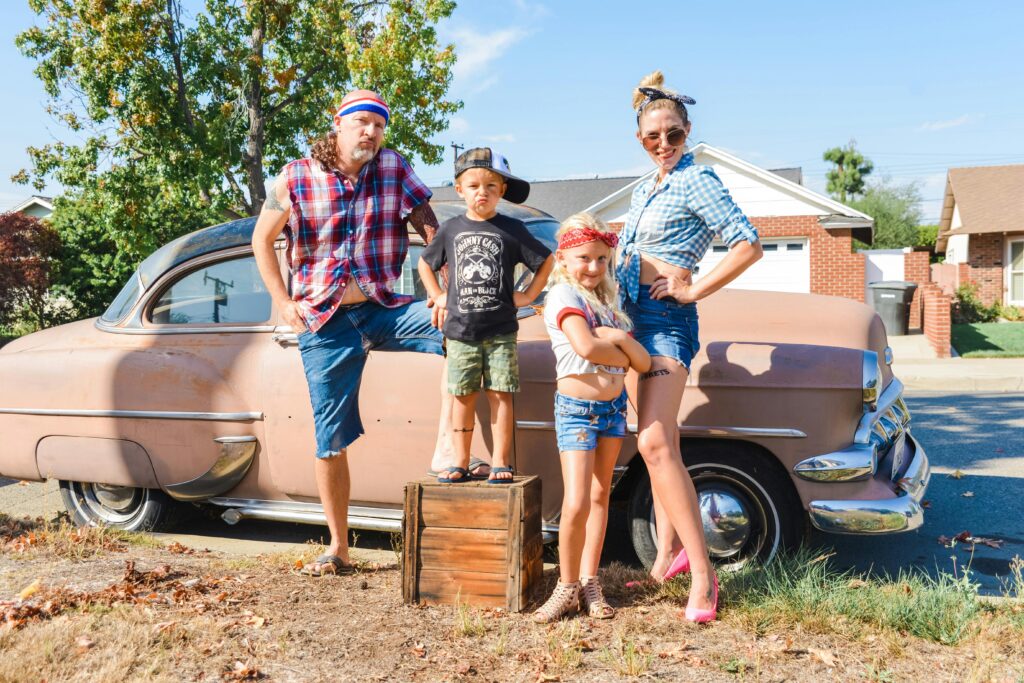 pexels photo 14212220 14212220 Family posing playfully with a vintage car on a sunny day.