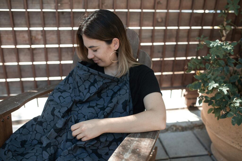 pexels photo 6849481 6849481 Mother sitting outdoors comfortably breastfeeding her baby under a stylish nursing cover.